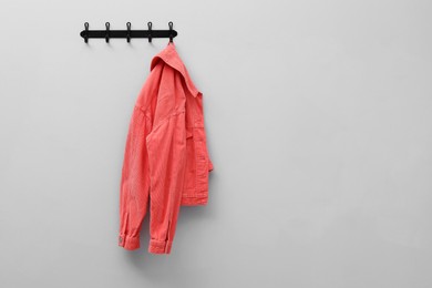 Photo of Coral jacket hanging on coat rack on light grey wall, space for text