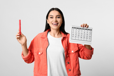 Photo of Young woman holding calendar with marked menstrual cycle days on light background