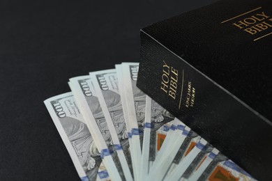 Photo of Holy Bible with money on black background, closeup
