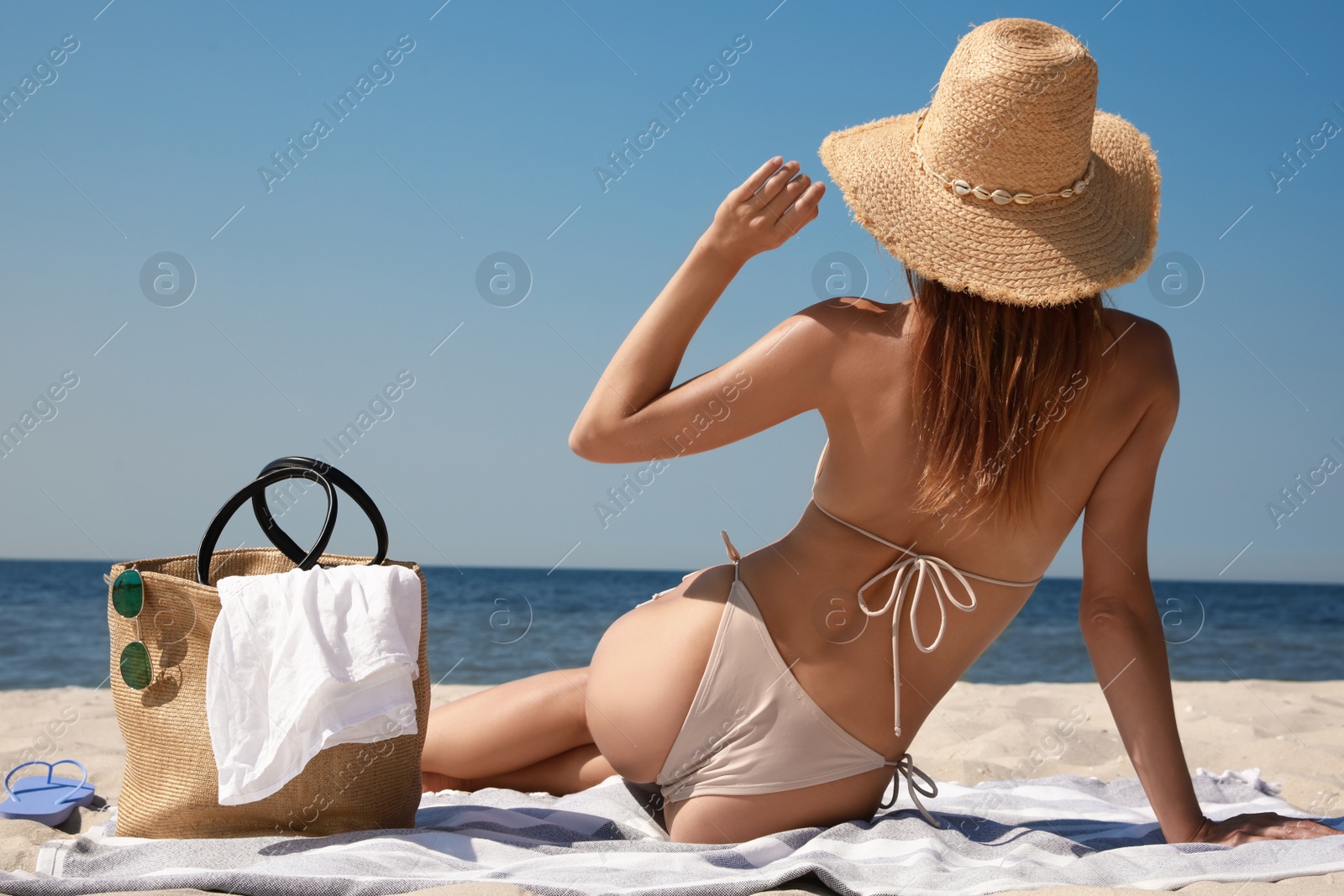 Photo of Woman with beach bag and straw hat on sand near sea, back view