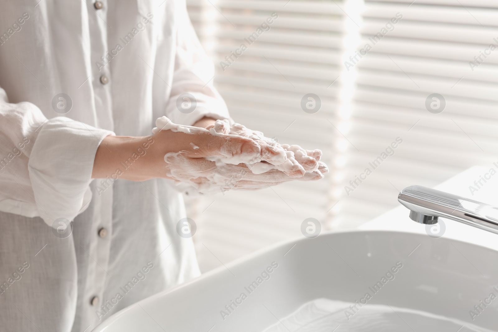 Photo of Woman washing hands with cleansing foam near sink in bathroom, closeup