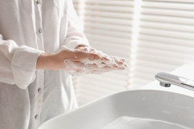 Woman washing hands with cleansing foam near sink in bathroom, closeup