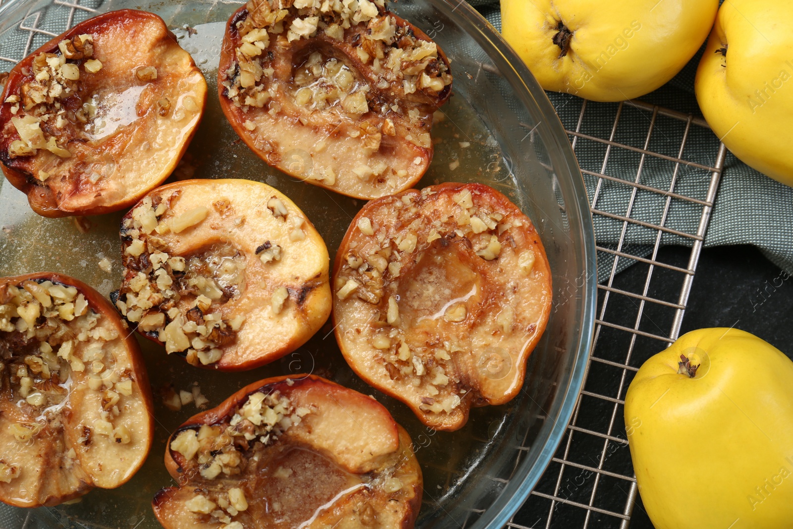 Photo of Tasty baked quinces with walnuts and honey in bowl on black table, flat lay