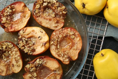 Photo of Tasty baked quinces with walnuts and honey in bowl on black table, flat lay