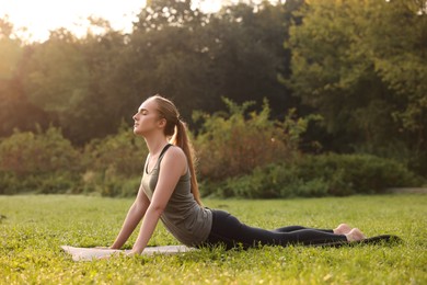 Beautiful woman practicing yoga on mat outdoors