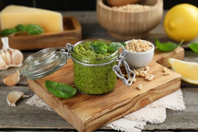 Photo of Delicious pesto sauce in jar and ingredients on wooden table