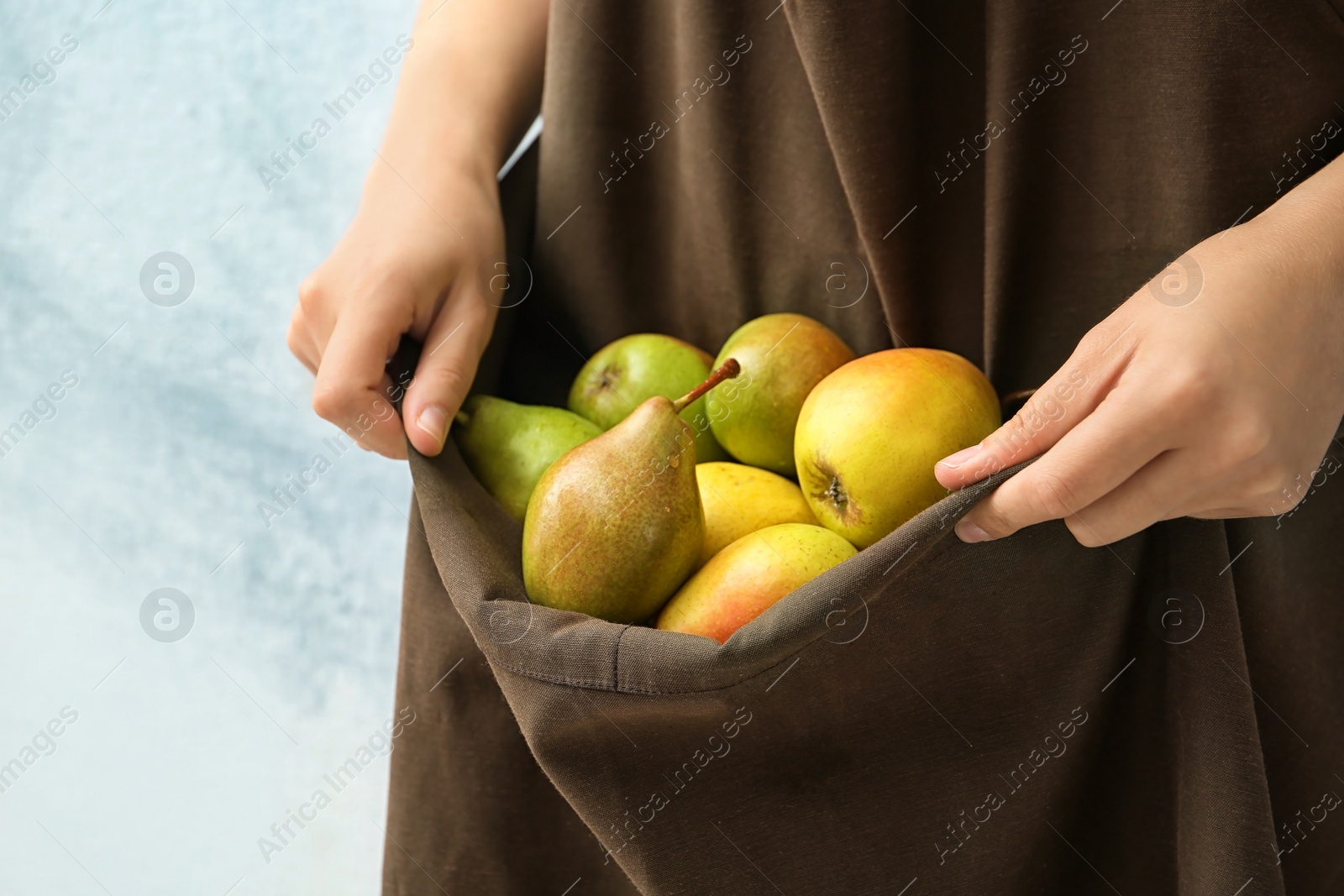 Photo of Woman in apron with ripe pears on color background, closeup