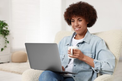 Photo of Young woman using laptop and drinking coffee in room, space for text