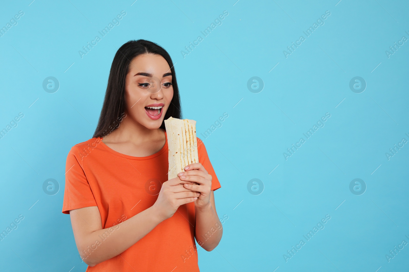 Photo of Young woman eating tasty shawarma on turquoise background. Space for text