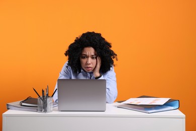 Stressful deadline. Sad woman looking at laptop at white desk on orange background