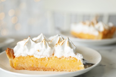 Plate with piece of delicious lemon meringue pie on white marble table