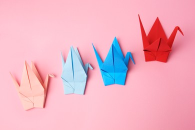 Colorful paper origami cranes on pink background, flat lay