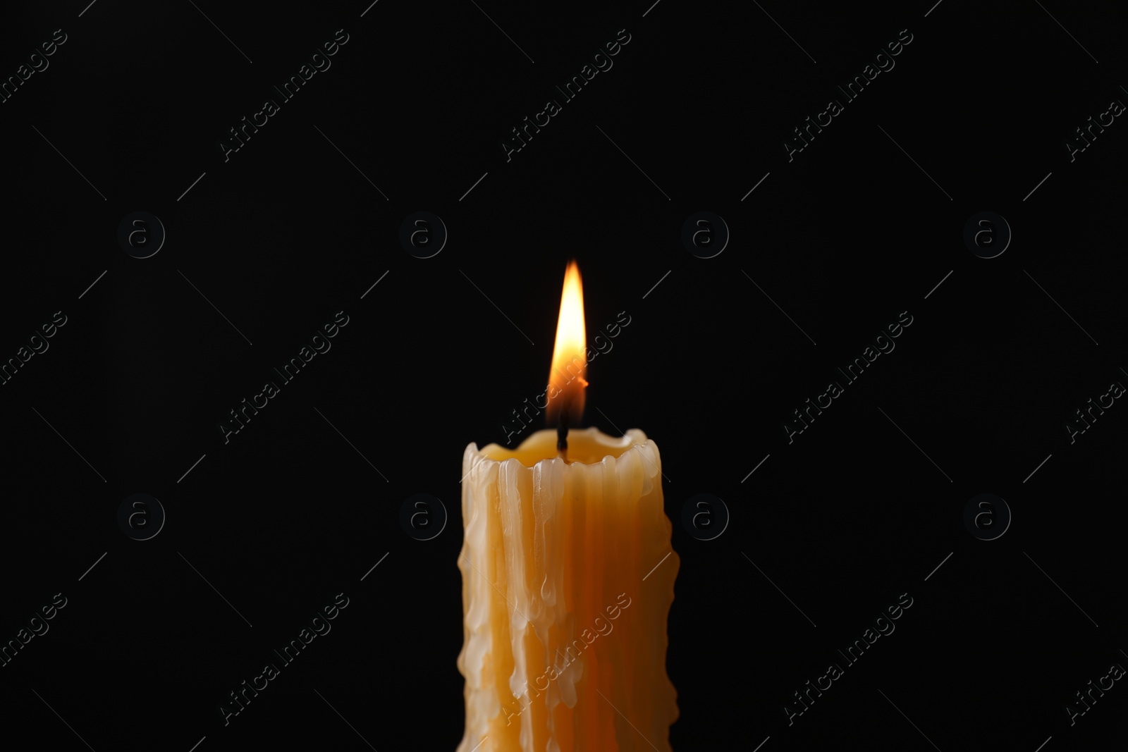 Photo of Burning church wax candle on black background, closeup