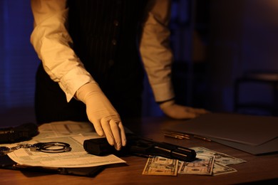 Photo of Professional detective in protective gloves working with evidence indoors at night, closeup