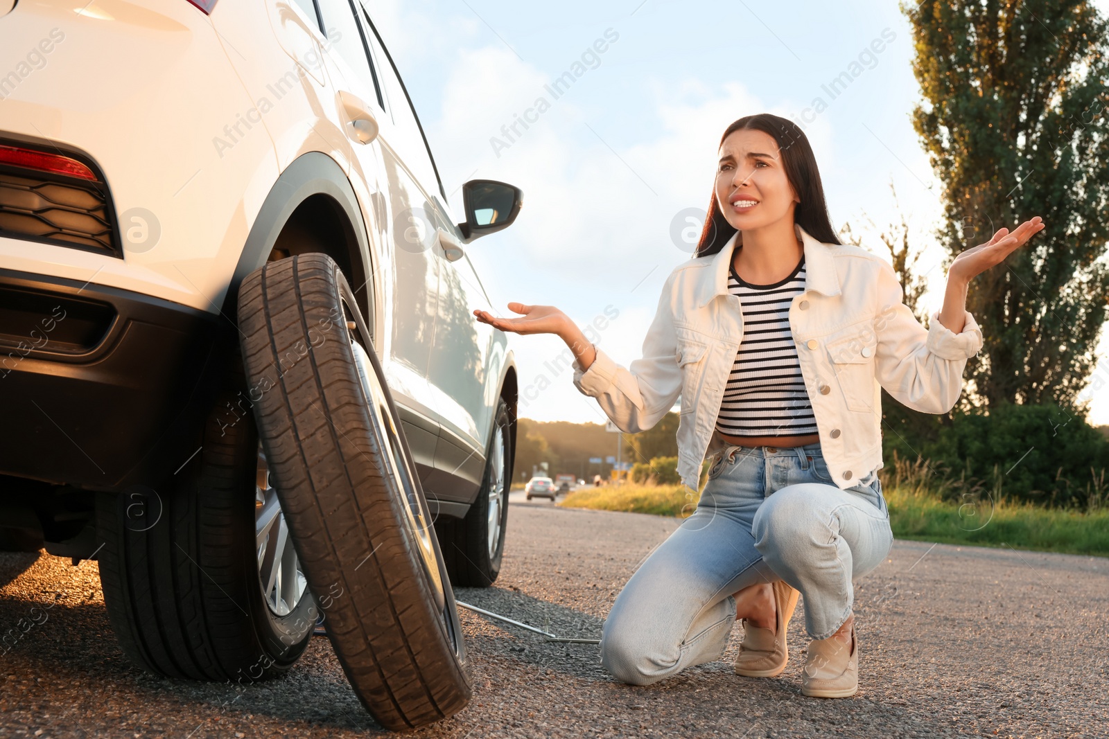 Photo of Worried young woman near car on roadside. Changing wheel