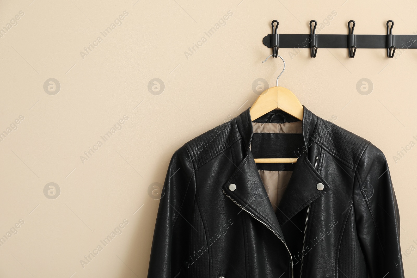 Photo of Hanger with black leather jacket on beige wall, space for text