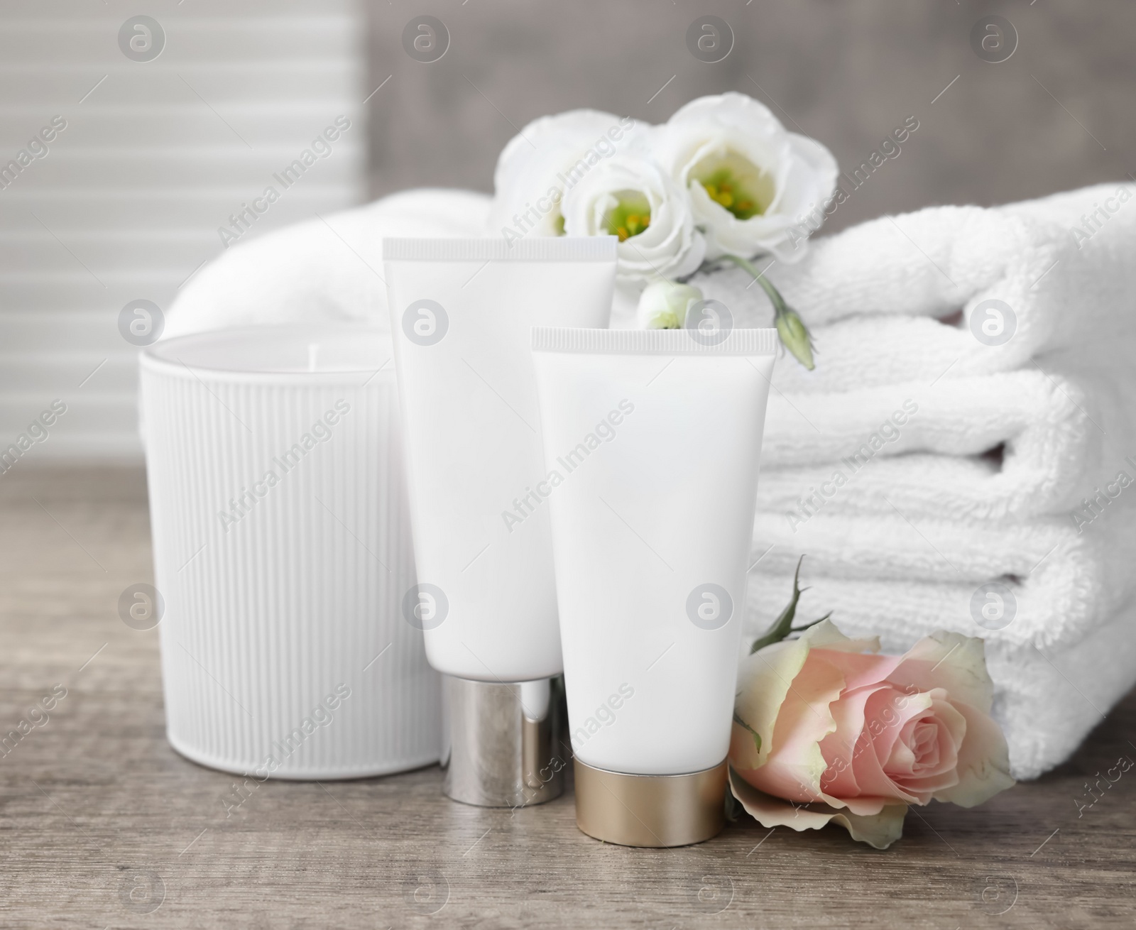 Photo of Cosmetic products, scented candle and folded towels with flowers on wooden table indoors