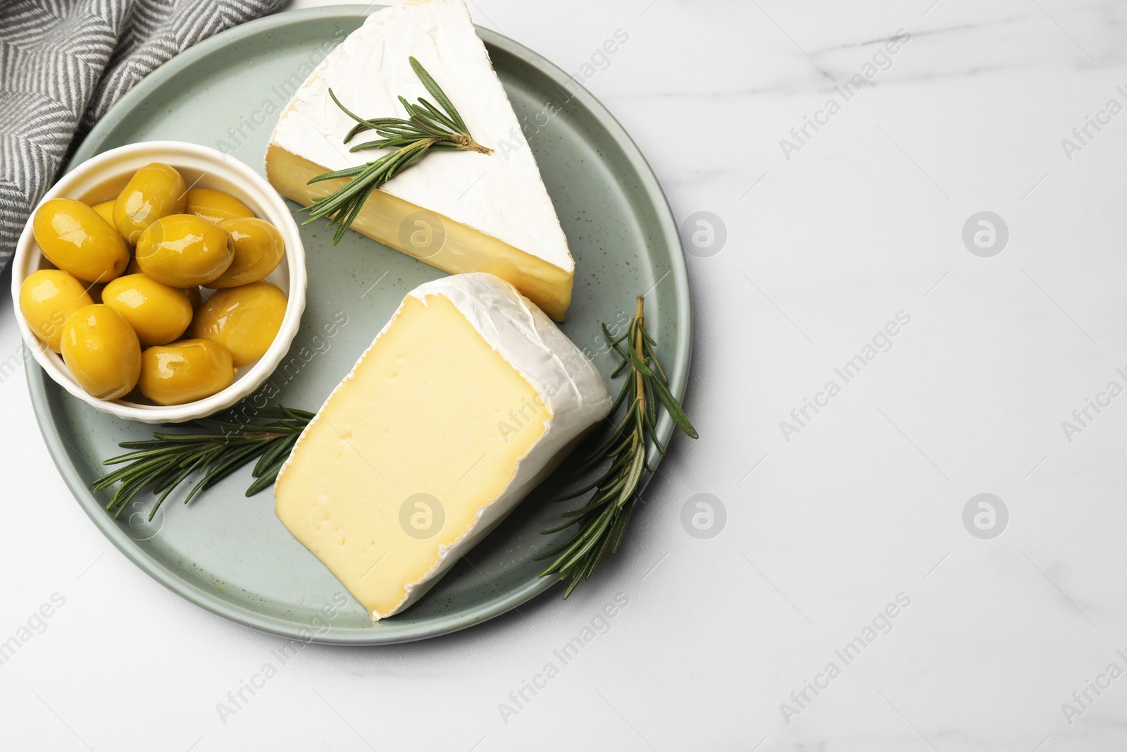 Photo of Plate with pieces of tasty camembert cheese, olives and rosemary on white table, top view. Space for text
