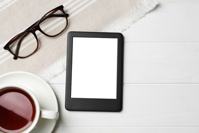 Photo of Modern e-book reader near glasses and cup of tea on white wooden table, flat lay. Space for text