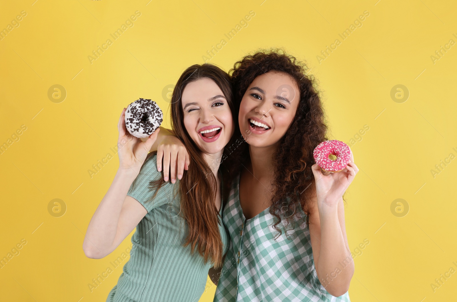 Photo of Beautiful young women with donuts on yellow background