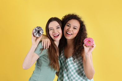 Beautiful young women with donuts on yellow background