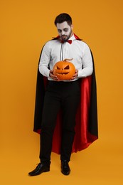 Man in scary vampire costume with fangs and carved pumpkin on orange background. Halloween celebration