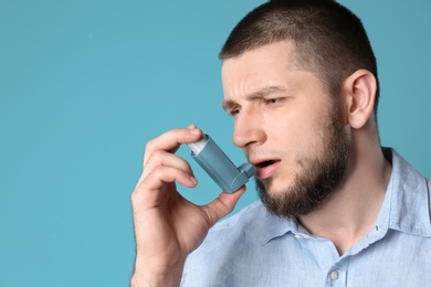 Young man using asthma inhaler on color background