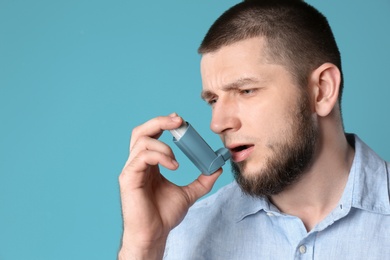 Photo of Young man using asthma inhaler on color background