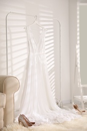 Photo of Beautiful wedding dress hanging on rack indoors