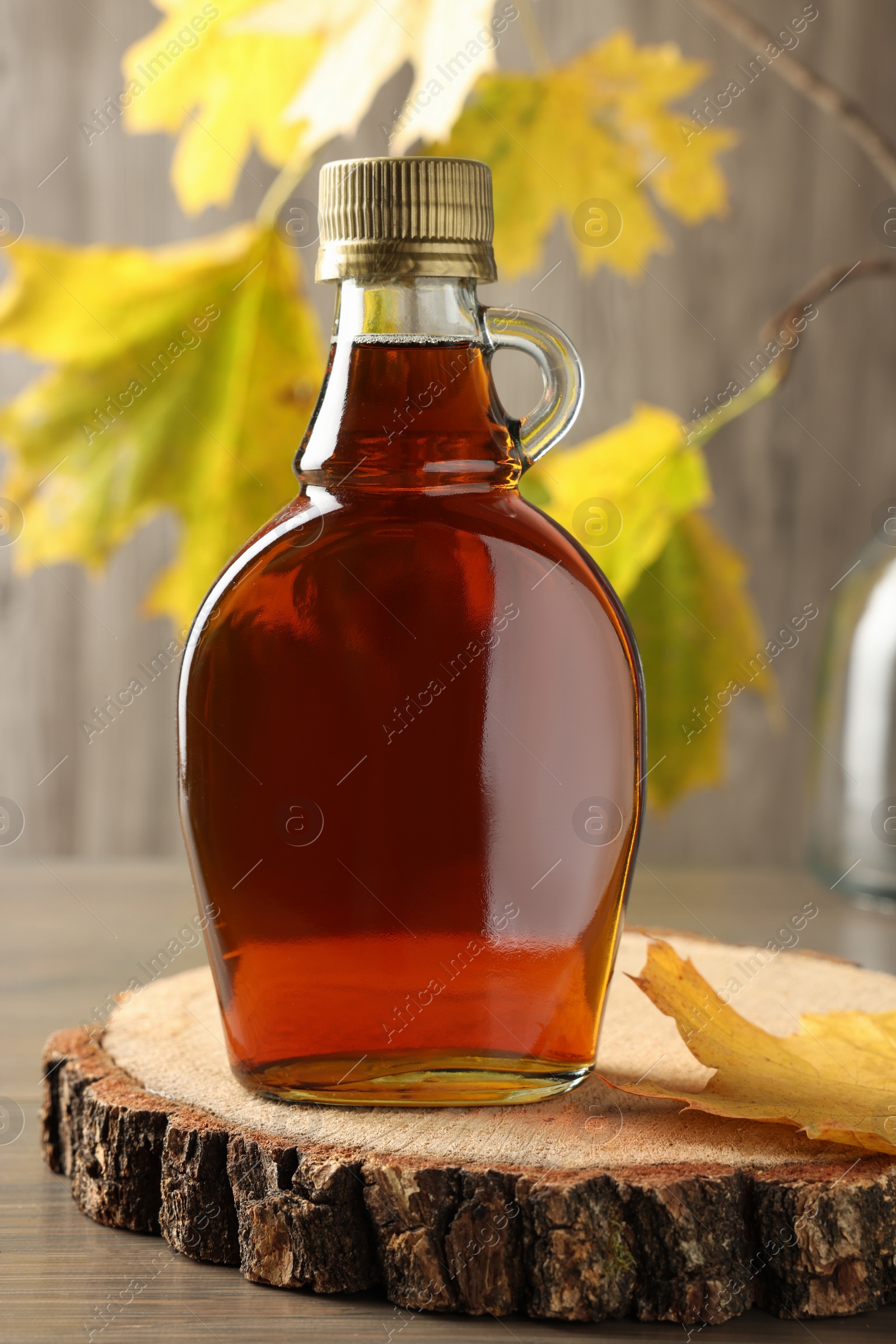 Photo of Bottle of tasty maple syrup and dry leaf on wooden table