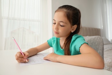 Little girl solving sudoku puzzle at table indoors