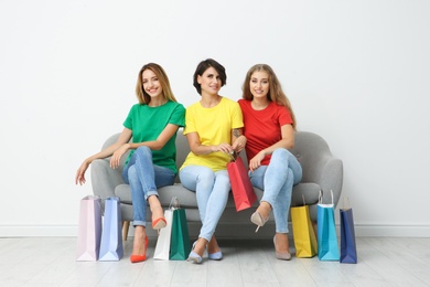 Photo of Group of young women with shopping bags sitting on sofa near light wall