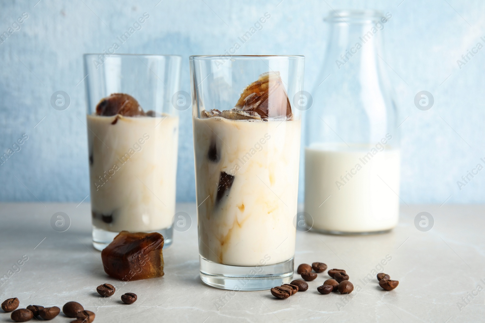 Photo of Glasses of milk with coffee ice cubes and beans on table against color background