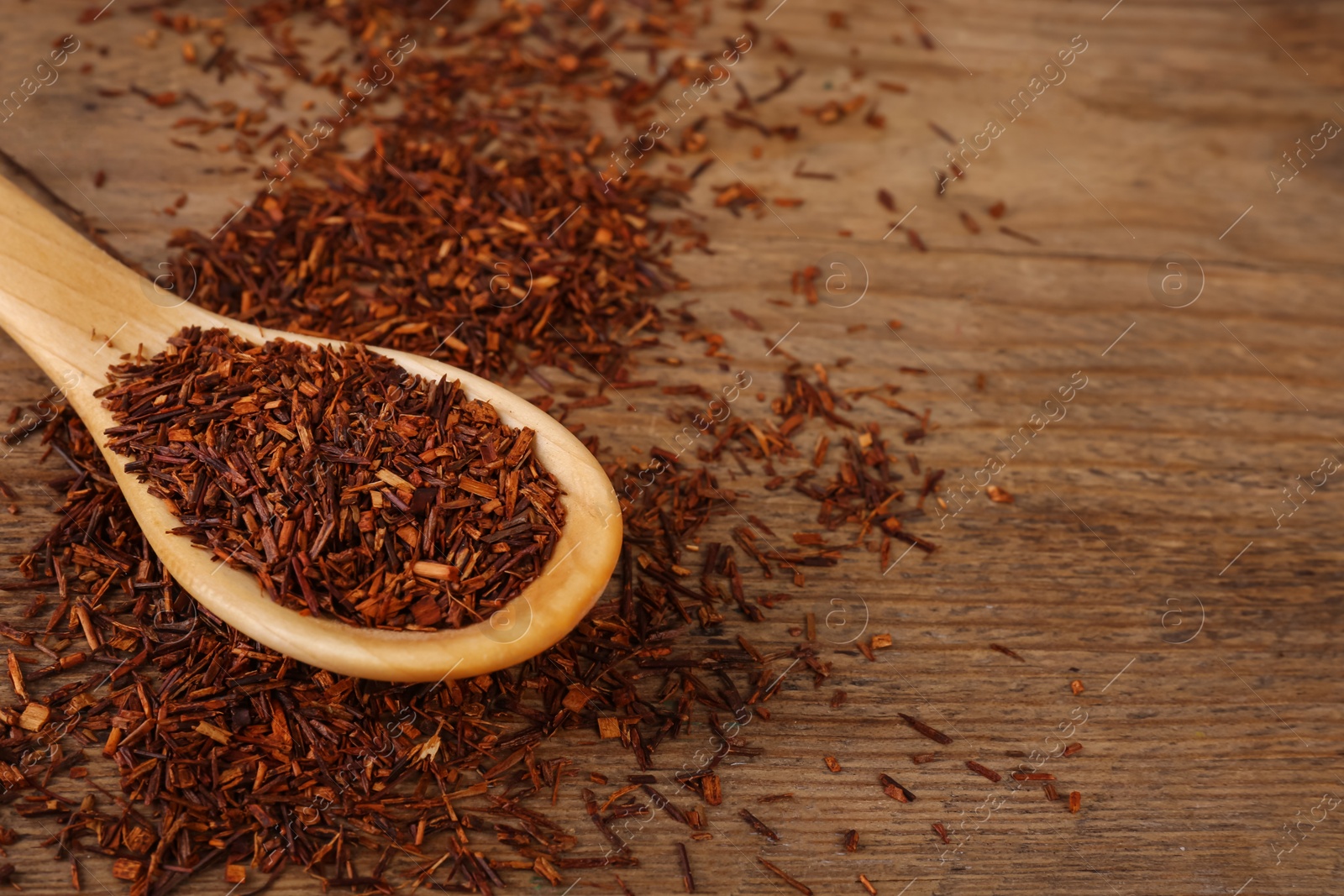 Photo of Spoon with dry rooibos leaves on wooden table, closeup. Space for text