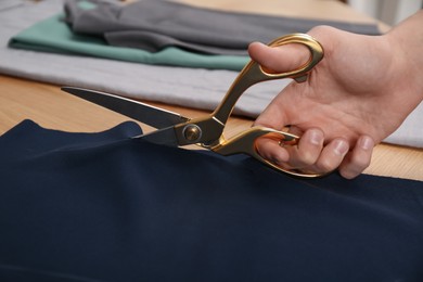 Photo of Man cutting blue fabric with scissors at wooden table, closeup