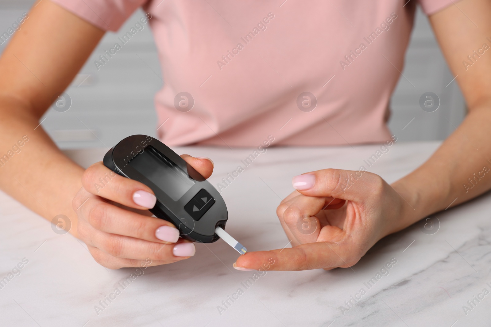Photo of Diabetes. Woman checking blood sugar level with glucometer at white marble table, closeup