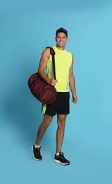 Handsome man with sports bag on light blue background