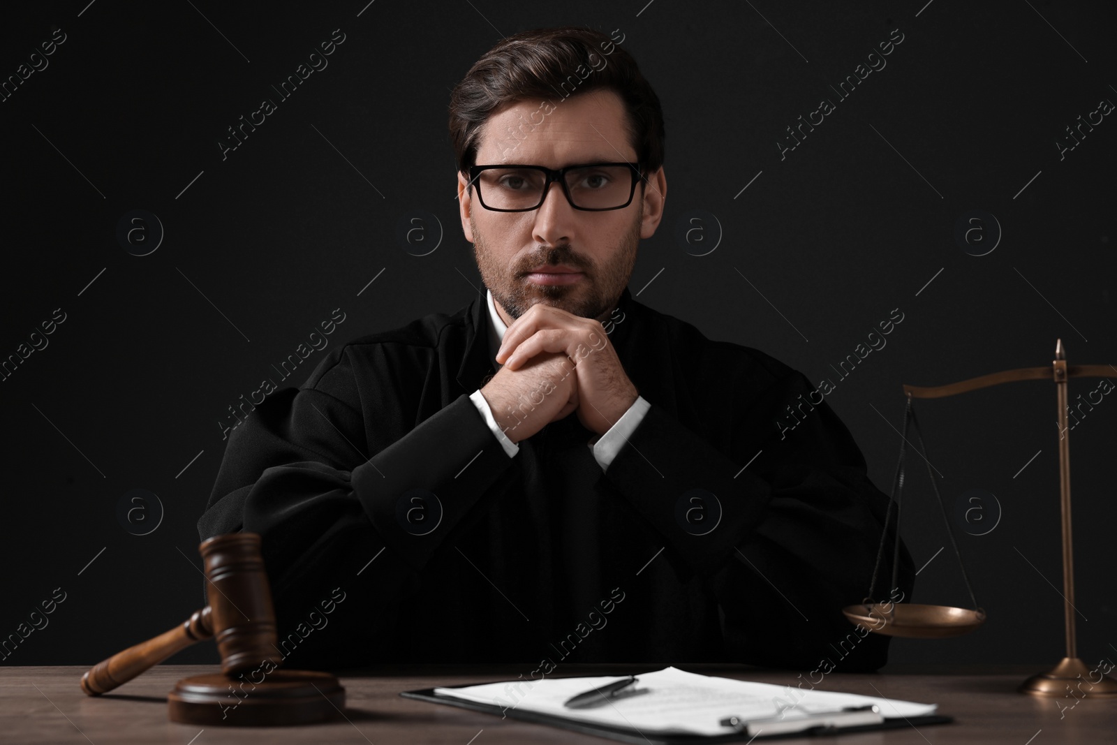 Photo of Judge with gavel and papers sitting at wooden table against black background