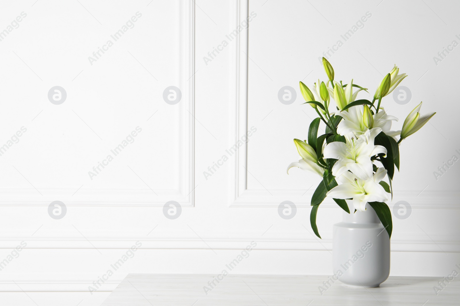 Photo of Beautiful bouquet of lily flowers in vase on light table near white wall, space for text