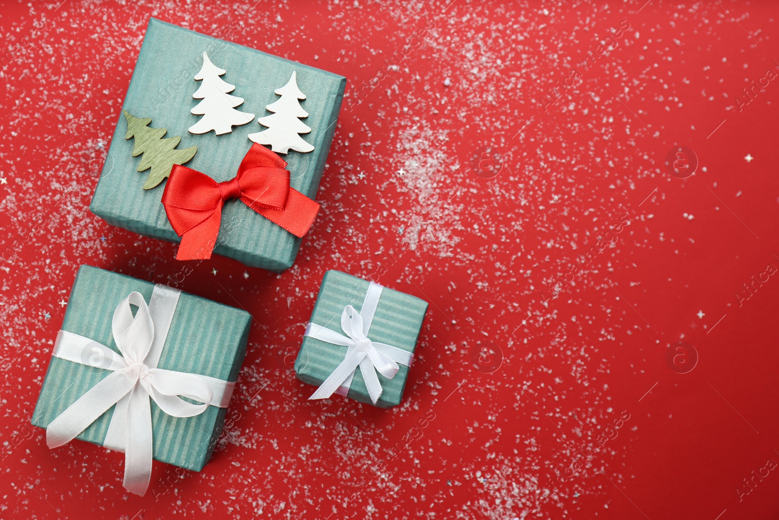 Photo of Christmas gift boxes with snow on red background, flat lay. Space for text