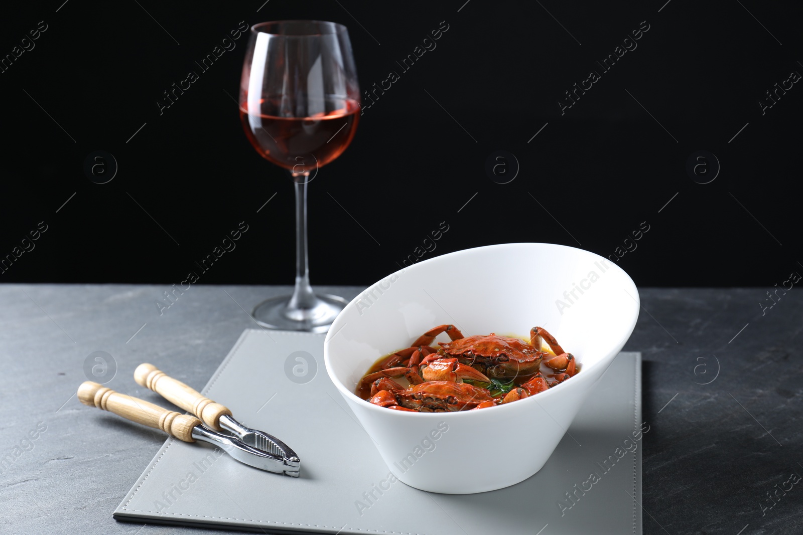 Photo of Delicious boiled crabs with sauce, glass of wine and cracker on grey table