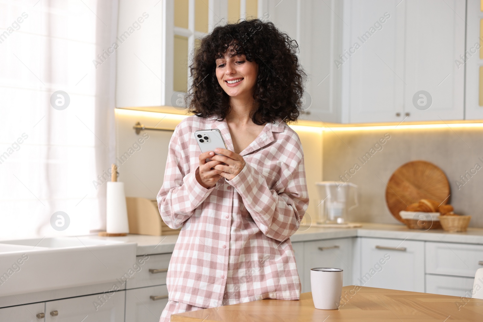 Photo of Beautiful young woman in stylish pyjama with smartphone in kitchen