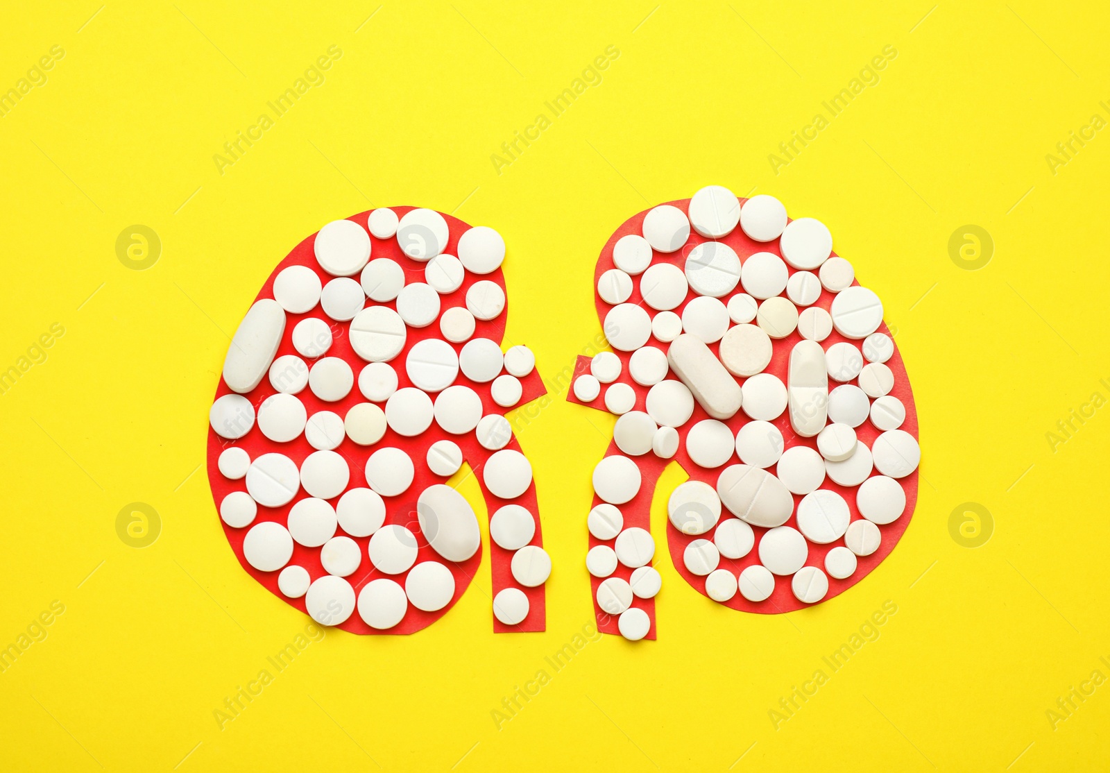 Photo of Paper cutout of kidneys with pills on yellow background, top view