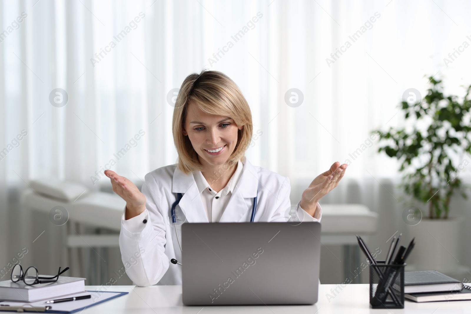 Photo of Smiling doctor with laptop having online consultation at table in office