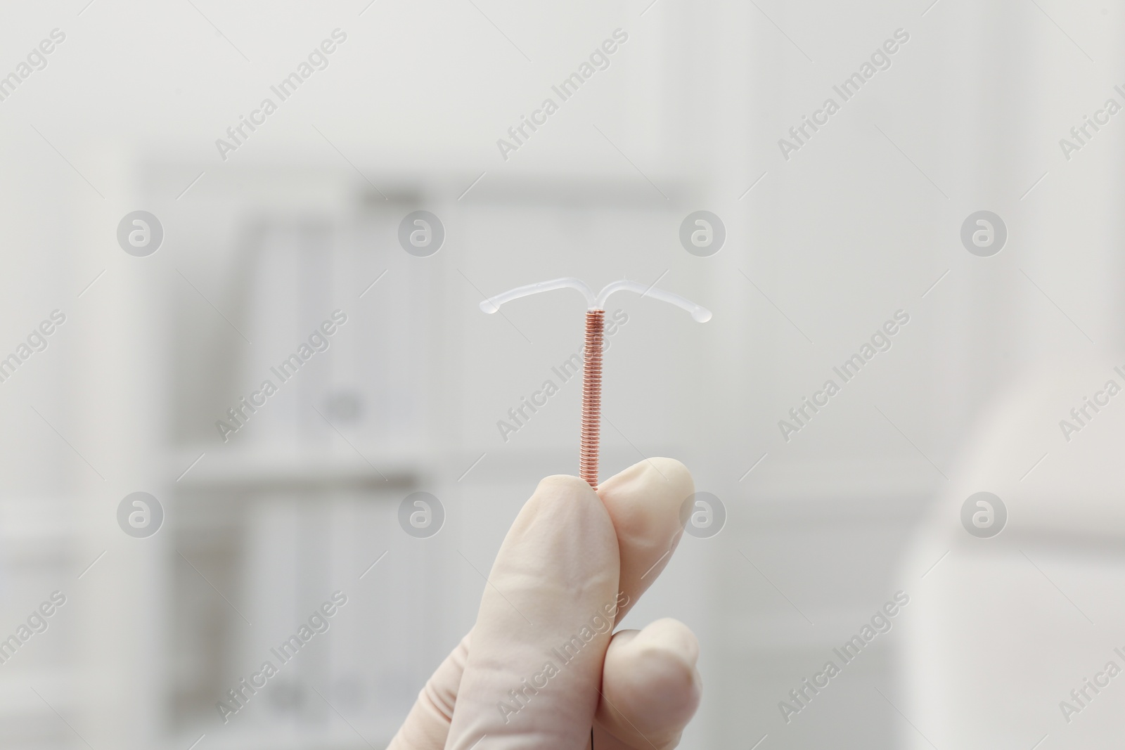 Photo of Doctor holding T-shaped intrauterine birth control device on blurred background, closeup