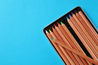 Photo of Box with many colorful pastel pencils on light blue background, top view and space for text. Drawing supplies