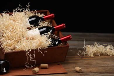 Box with wine bottles on wooden table against black background. Space for text