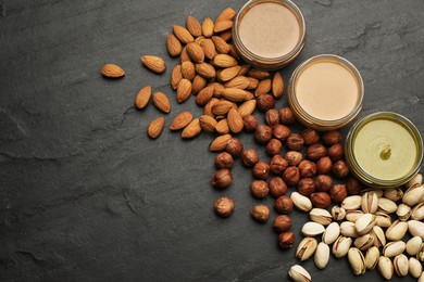 Photo of Different types of delicious nut butters and ingredients on black table, flat lay. Space for text