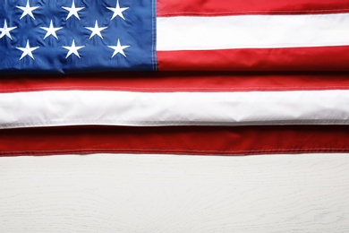 Folded American flag on wooden background, top view with space for text