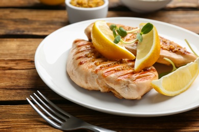 Photo of Tasty grilled chicken fillets with green sprouts and lemon slices on wooden table, closeup
